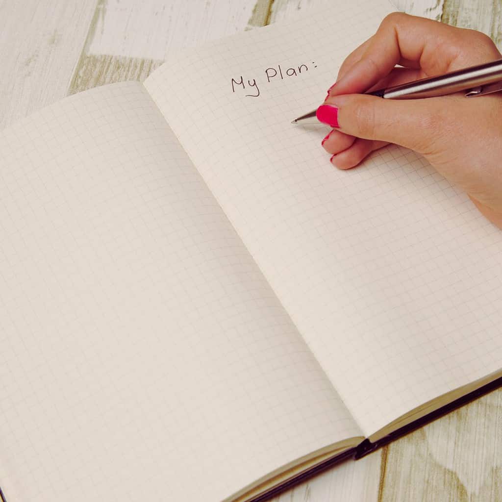 Produktiv durch einen Tagesplan - Frauenhand mit Stift auf kariertem Notizbuch auf dem "My Plan" geschrieben steht