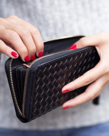 Geld ausgeben - Frauenhände mit roten Fingernägeln halten ein schwarzzes Leder